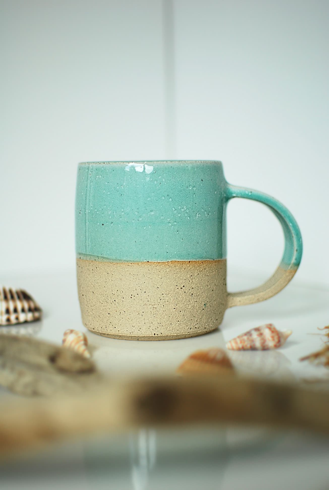 A two-tone Verdon mug with a layered celadon glaze over glossy white on the upper half and raw speckled clay at the base.