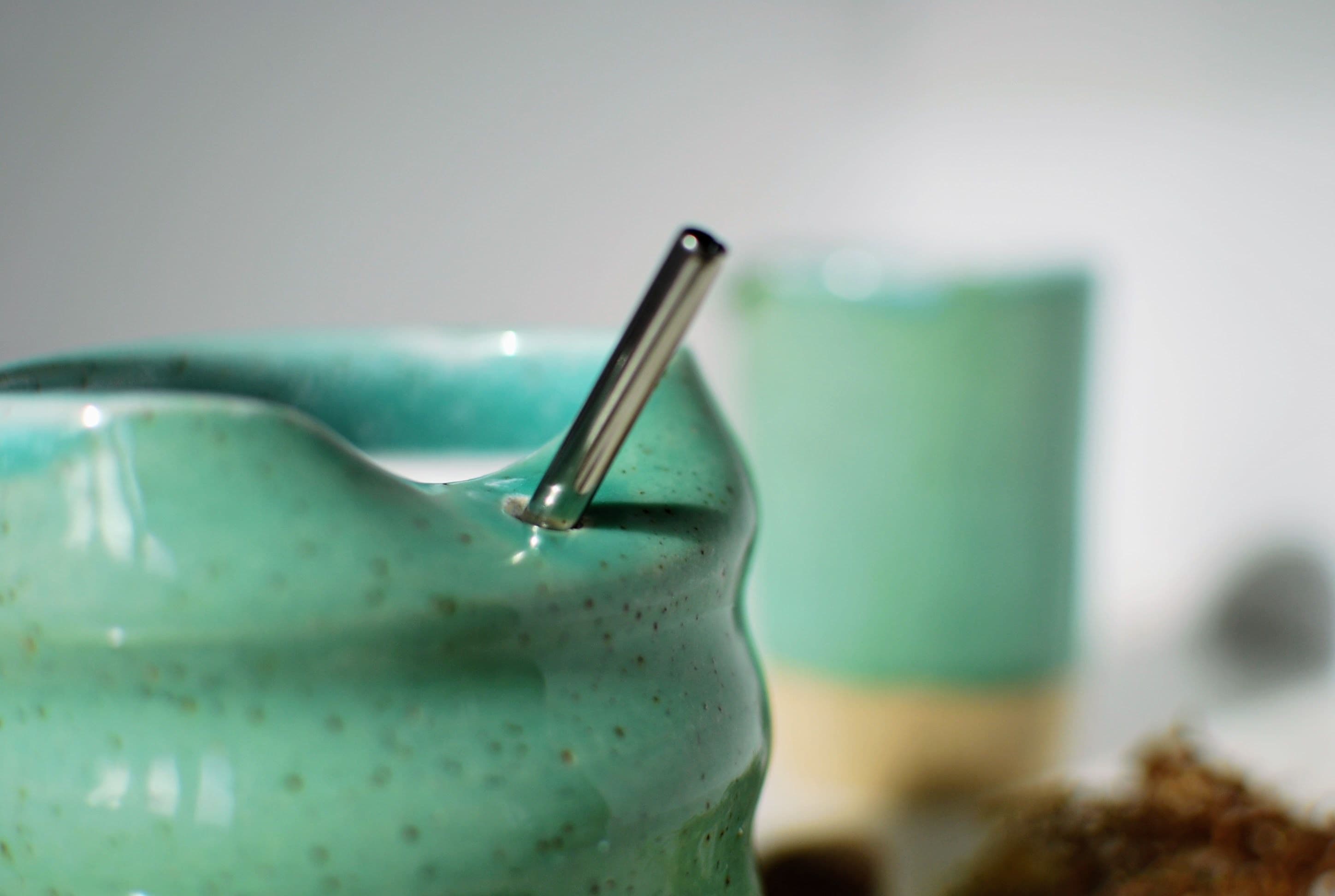 Close-up of a wheel-thrown stoneware tumbler, soft aqua glaze over speckled natural clay base, with stainless steel straw — Maguelone collection, made in Dublin, Ireland