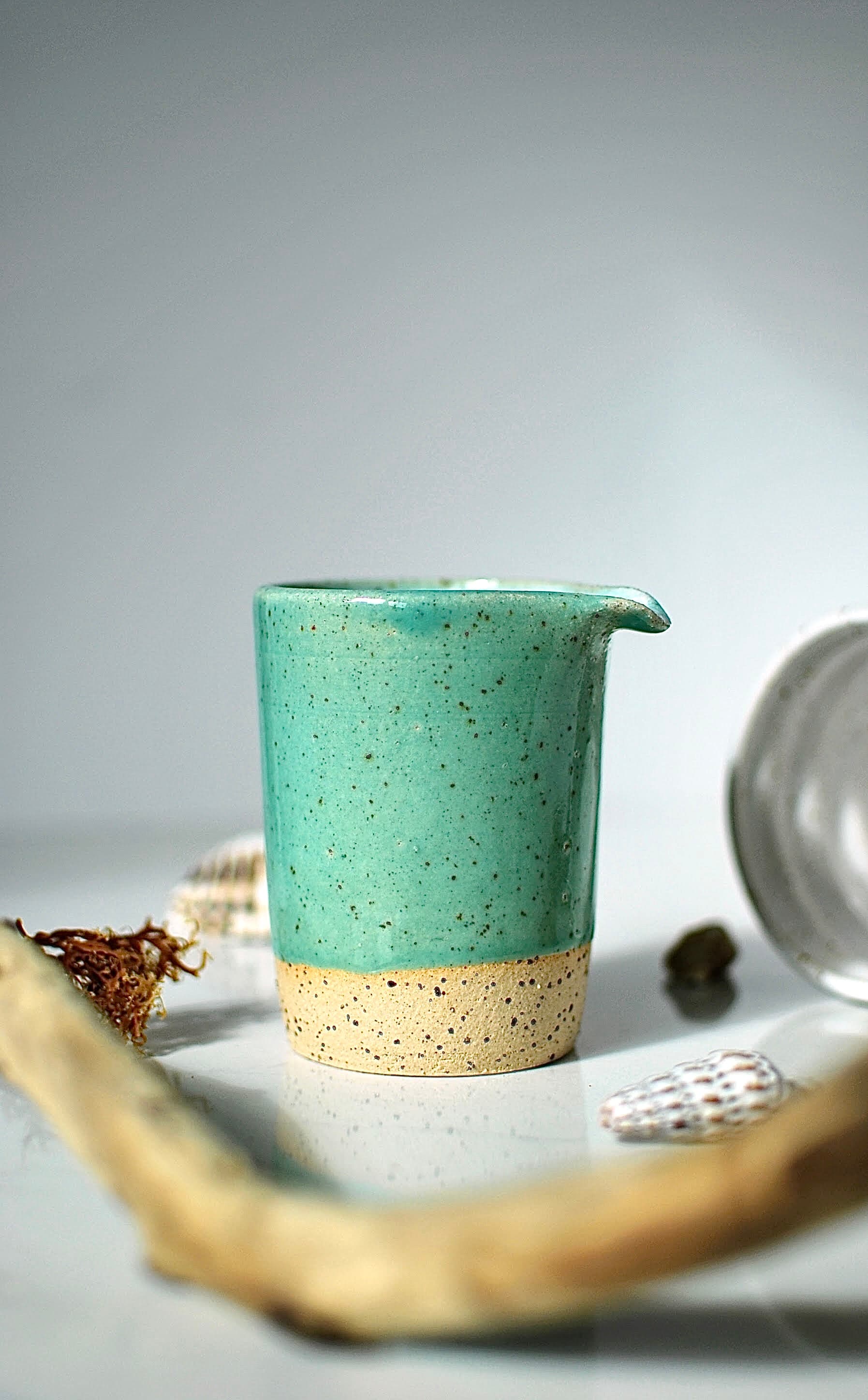 Handmade stoneware milk jug with glossy turquoise speckled glaze, styled with driftwood and seashell β Maguelone collection, Studio Lippi Ceramics in Dublin