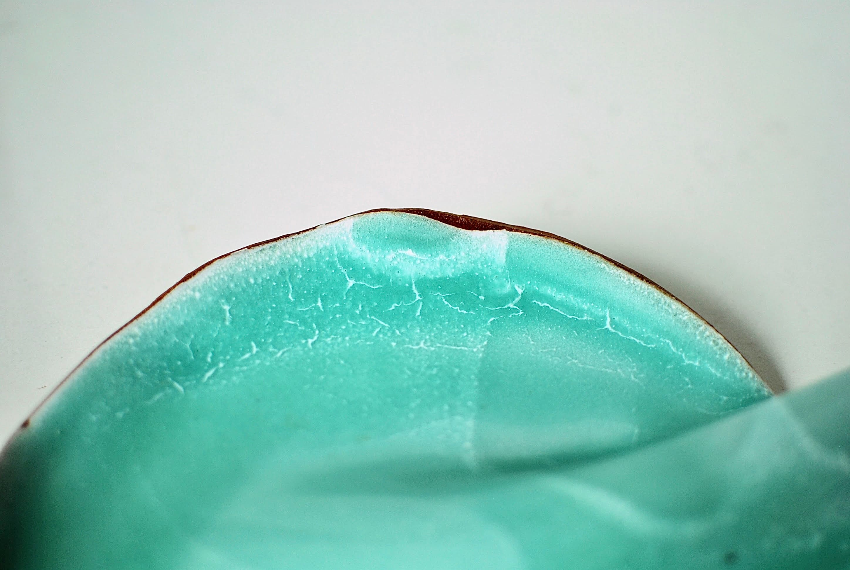 Close-up of the curved edge of a handmade turquoise ceramic charcuterie board made in Dublin, Ireland from sandy-coloured stoneware clay.