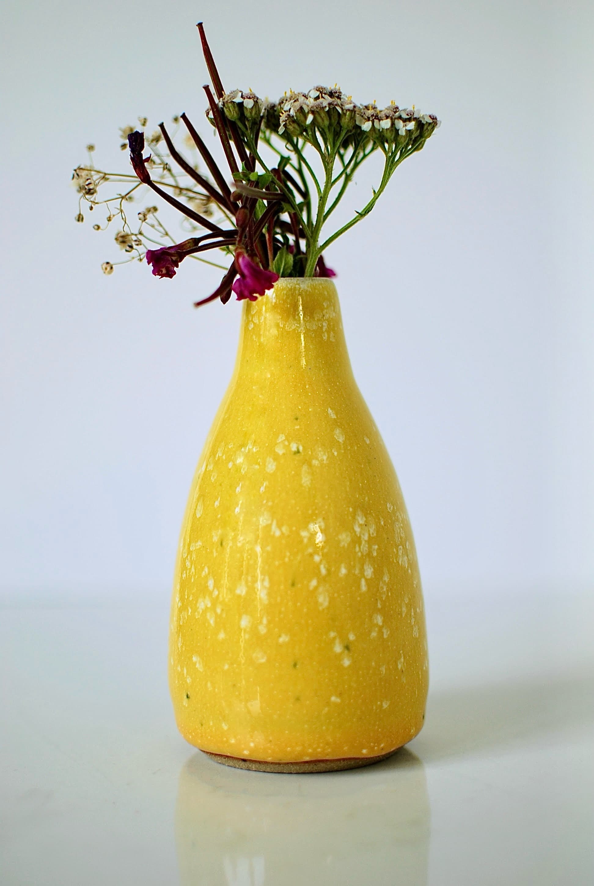 Small yellow ceramic vase with a narrow neck, glossy speckled finish and wildflowers, handmade in Dublin